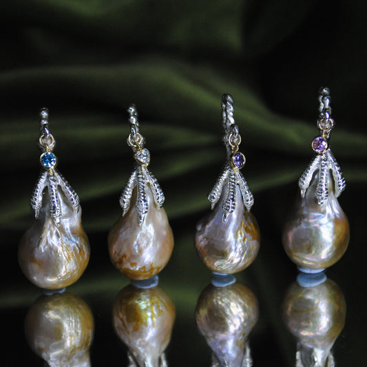 Set of four pearl charms with decorative elements on a reflective surface.