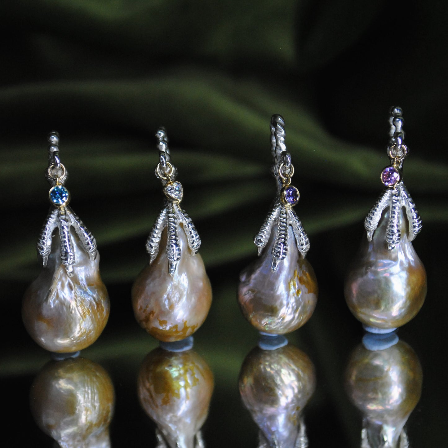Set of four pearl charms with decorative elements on a reflective surface.