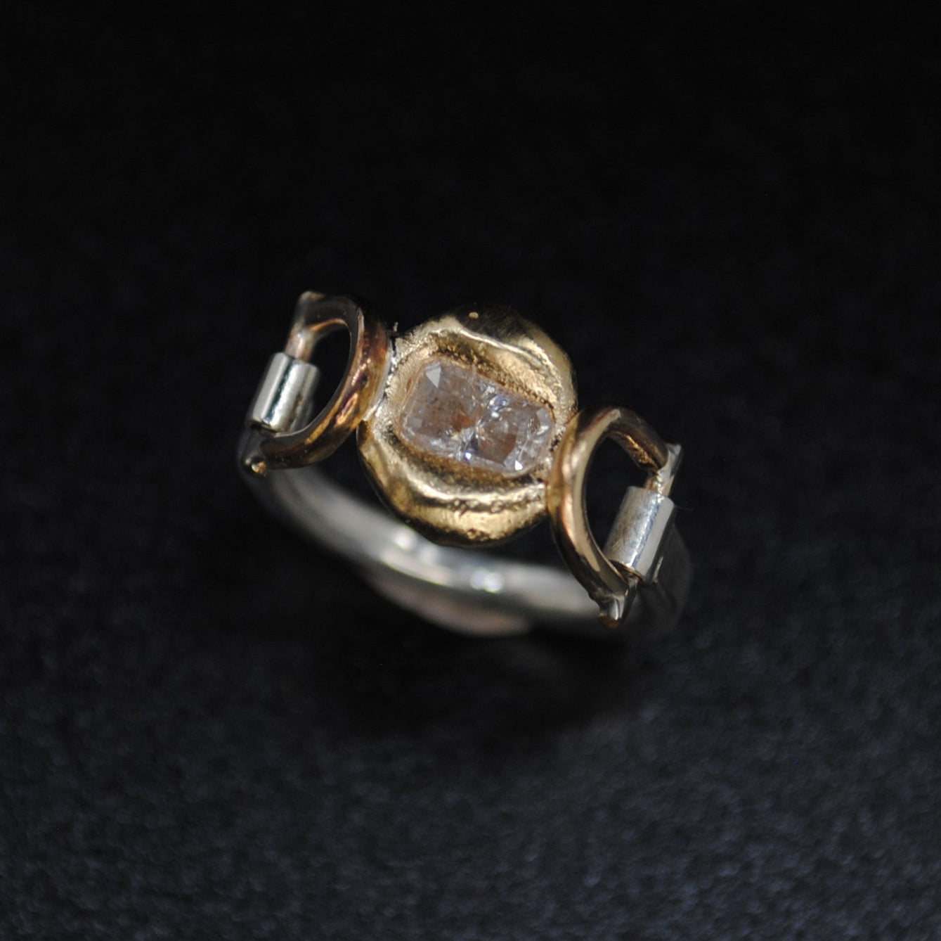 Gold and silver ring with a diamond on a dark textured background