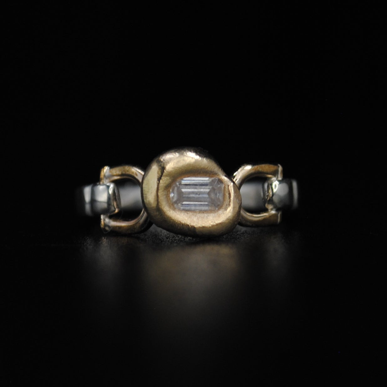 A gold and silver ring with a central oval gold setting and side loops, photographed on a solid black background.