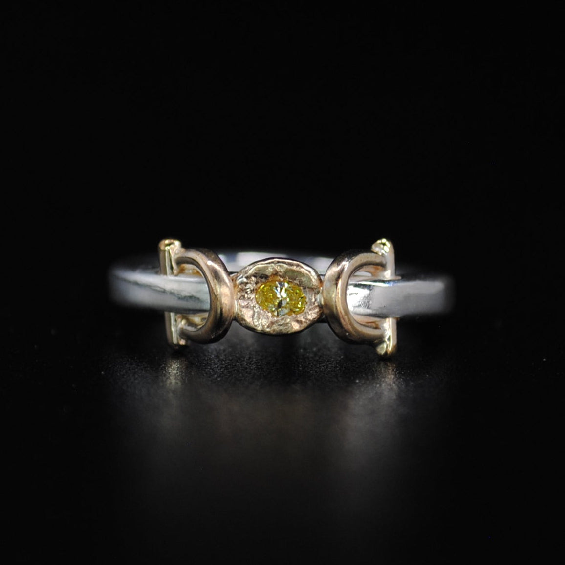 A delicate two-tone ring featuring a central round yellow gemstone flanked by crescent moon motifs in yellow gold and silver, set against a solid black background.